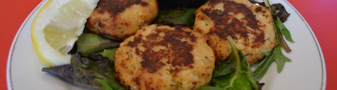 Three golden crab cakes served with dipping sauce and lemon on a bed of greens.