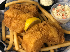 Basket of fried fish, French fries, and coleslaw with tartar sauce and lemon wedge.